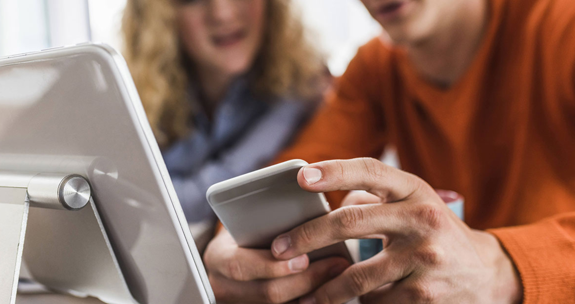 Zwei Kollegen am Schreibtisch mit Handy und Tablet