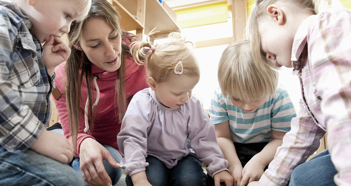 Erzieherin und Kinder sehen sich ein Bilderbuch an