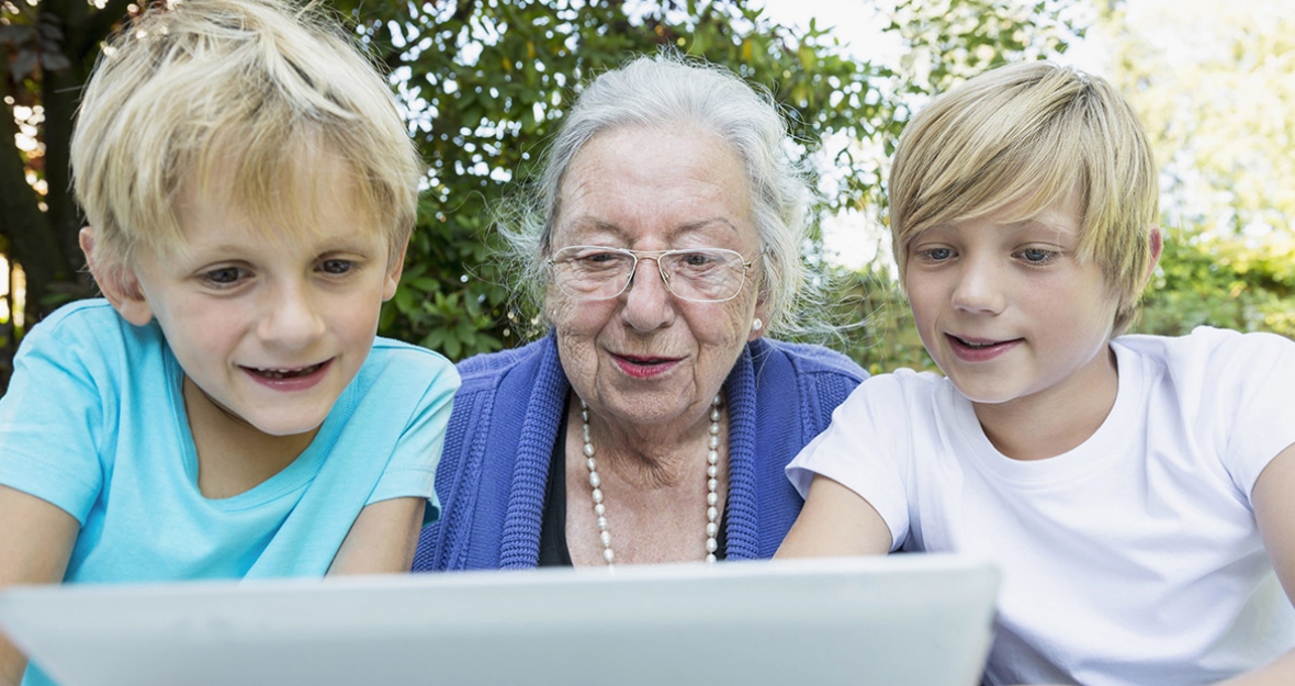 Großmutter sitzt mit ihren Enkeln vor einem Tablet