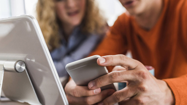 Zwei Kollegen am Schreibtisch mit Handy und Tablet