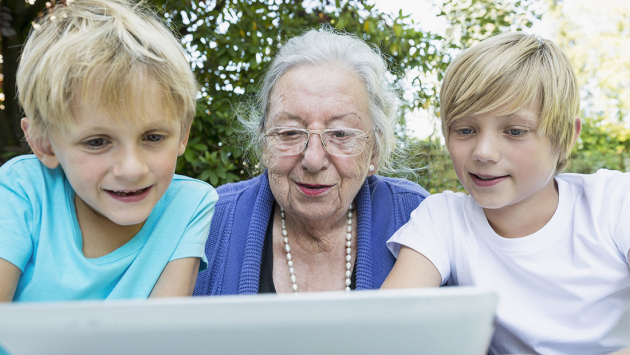 Großmutter schaut mit ihren zwei Enkeln auf einen Laptop