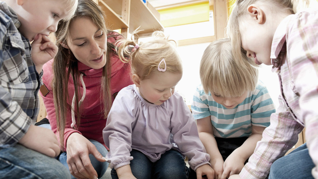 Erzieherin und Kinder sehen sich ein Bilderbuch an