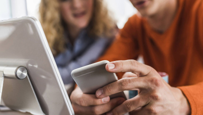 Zwei Kollegen am Schreibtisch mit Handy und Tablet